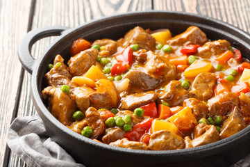 One pot of beef with potatoes, carrots, tomatoes, green peas, onions with spicy sauce close-up in a frying pan on a wooden table. Horizontal