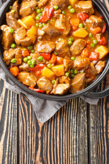 Homemade beef stew with seasonal vegetables close-up in a saucepan on a wooden table. Vertical top view from above