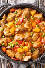Beef stew with potatoes, carrots, green peas and spices close-up in a frying pan on a wooden table. Vertical