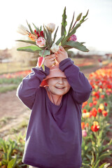 Young preteen girl stretching bunch of tulips to the camera, sunset outdoor scene. - 587053816