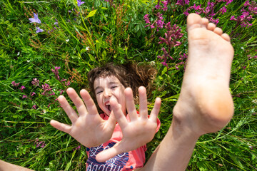 Portrait of a child girl in summer lying in the grass and wildflowers with heels and palms. summer...