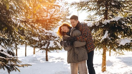 Smiling spouses spend a day off in a sunny snowy park. Young people spend a romantic date in...