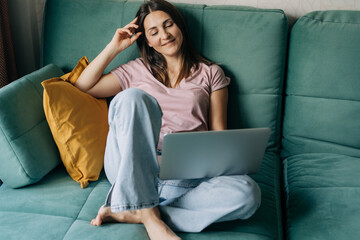 Happy smiling woman in her forties sitting on sofa at home working using laptop.