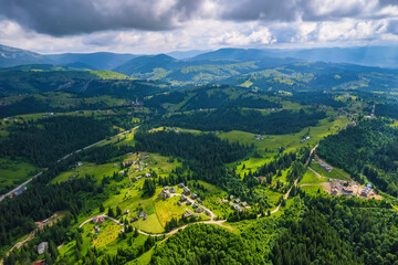 Fototapeta na wymiar Scenic aerial view of the Carpathian mountains, village and blue sky with sun and clouds in morning light, summer rural landscape