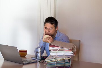 Obraz premium Image of a desperate man holding a sandwich and a small bottle of water who has to work overtime in his office due to overwork.