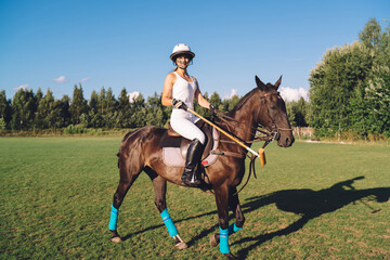 Graceful female polo player riding horse on field under blue sky