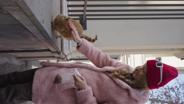Kind girl in feeding a homeless three-legged cat on the street, vertical video