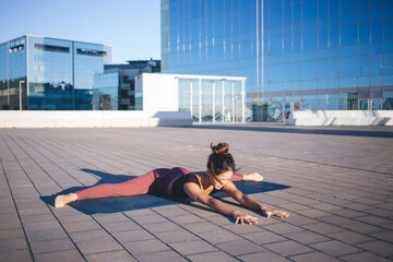 Asian fit trainer practice twine method during morning warm up at urban setting enjoying healthy lifestyle, experienced woman in tracksuit stretching flexible muscles during hatha workout outdoors