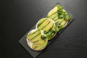 Round crispy rice crackers with avocado on black board background.