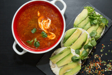 Red borscht (borsch) and round crispy rice crackers with avocado. on black board background. Ukrainian national traditional dish
