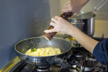 Image of a woman's hands seasoning freshly cooked pasta in a pan with a pepper mill. Italian culinary tradition.
