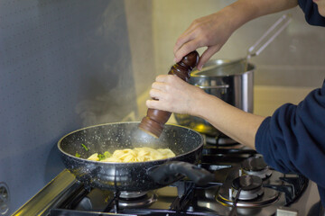 Image of a woman's hands seasoning freshly cooked pasta in a pan with a pepper mill. Italian culinary tradition.
