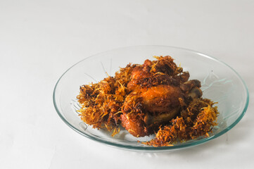 fried chicken with serundeng, which is grated coconut that is fried and seasoned, served on a small plate isolated on a white background