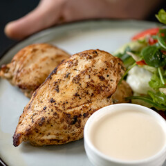 Baked chicken breast. Poultry meat with sauce and salad on white plate. Chicken fillet. Healthy food. Low calorie food. Healthy lifestyle. Fitness menu. Close-up. Top view. Soft focus. 