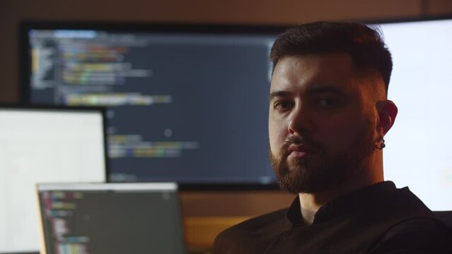 Portrait shooting of a young IT specialist. A web developer is sitting in his office in front of multiple monitors.