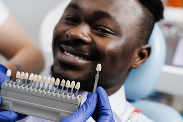 Teeth color shades guide close-up. African man in dentistry. Veneers or implants teeth color...