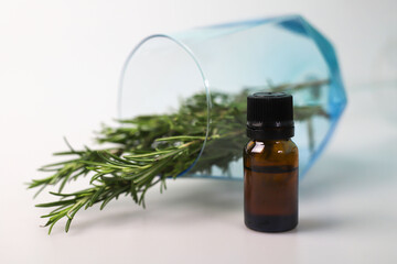 fragrant medicinal evergreen rosemary on a light background with a transparent glass and a jar of hair oil. medical plant rosemary for stress anxiety and more