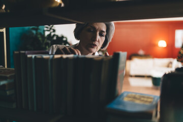 Obraz na płótnie Canvas Focused mature woman searching books row in shelf