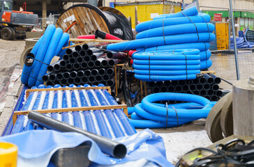 Blue and black pipelines of various diameters, concrete products and cables lie on a construction site on the street.