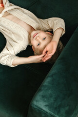 Portrait of a boy in a beige bathrobe, who lies on a green sofa and looks at the camera