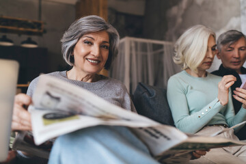 Smiling senior woman with newspaper relaxing on sofa with friends