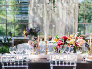 Served banquet table in the greenhouse. Bouquets with flowers, a glass of wine, dishes are on the table. In the background there is a panorama window and a view of the park.