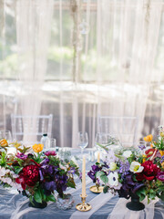 Served banquet table in the greenhouse. Bouquets with flowers, a glass of wine, dishes are on the table. In the background there is a panorama window and a view of the park.