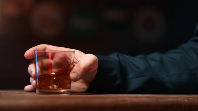 Businessman hand holding whiskey alcohol glass with ice cubes on wooden table bar pub party closeup