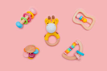 Cute set of wooden rattles for baby on pink background. Eco-friendly toys for newborns in the colors of the rainbow. Flat lay.