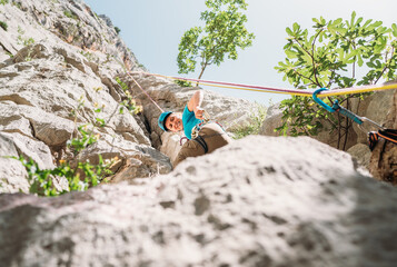 Smiling athletic woman in protective helmet climbing cliff rock wall using top rope and climbing...
