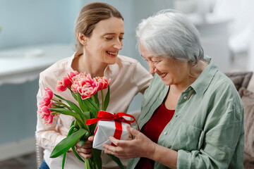 Happy Mother's Day. The daughter congratulates her mother and gives her a gift and a flowers