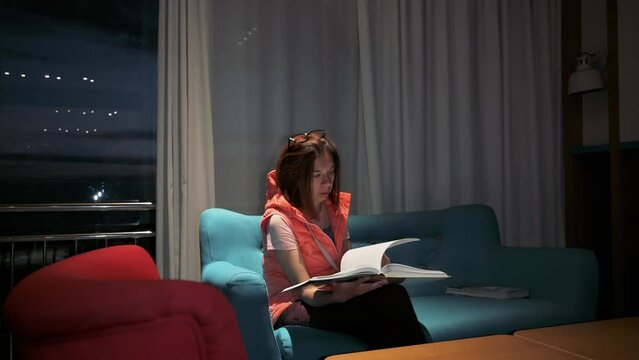 Woman reading a book siiting on sofa at night. 4k footage UHD 3840x2160 