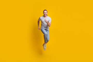 Fototapeta na wymiar Full length photo of pretty impressed man wear grey t-shirt running fast jumping high isolated yellow color background