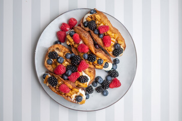 Fresh sweet rolls with cream cheese and fresh blueberries, strawberries, raspberries and currants on a white plate on a white-grey stripped surface. Copyspace. Food poster.