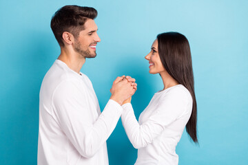 Profile portrait of two idyllic peaceful people hold hands toothy smile look each other isolated on blue color background © deagreez