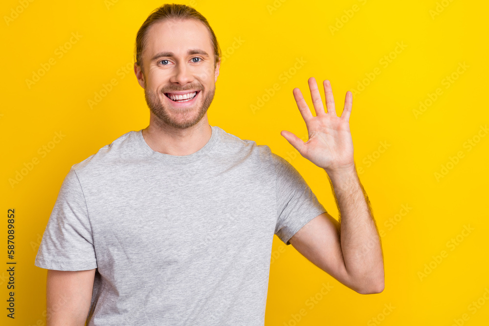 Sticker Photo of friendly funny guy dressed grey t-shirt waving arm palm isolated yellow color background