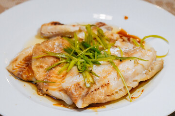 Steamed fish in black bean sauce arranged in a white plate