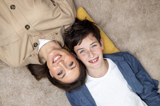 Portrait of happy woman with son, mother and boyfriend smiling and looking at camera lying together on carpets on floor at home in living room, having fun together.