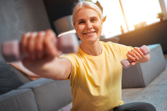 Portrait Of Beautiful Athletic Older Woman Holding Dumbbells Looking At Camera And Smiling. Active Lifestyle, Maintaining Health, Sport.