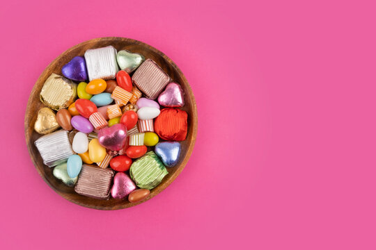 Bowl of candies, top view photo of bowl of candies. Colorful sweets in the wooden plate. Isolated pink background, copy space for greetings. Wrapped luxury chocolate. Ramadan feast celebration concept
