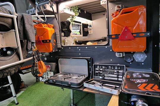 Rear part of custom motorcycle sport designed camper van Crawler TRC 458 by czech company MrKey, with jerrycans, grille accessories and part of interior visible. Caravan bike travel expo Nitra 2023.