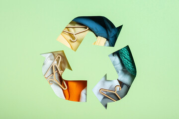 Colorful clothes and mini hungers under paper cut recycling symbol. Second hand, circular fashion...