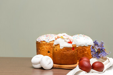 Easter holiday food concept. Homemade Easter cake with white icing, jelly candies, sweet powder, marsmallow, decorated with colored eggs, flowers blossoms on wooden background with copy space