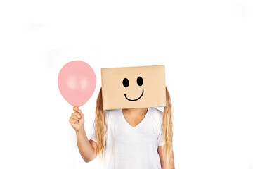 Mujer sonriente con una caja de cartón en la cabeza  sosteniendo un globo rosa pastel sobre un fondo blanco liso y aislado. Vista de frente y de cerca. Copy space - obrazy, fototapety, plakaty