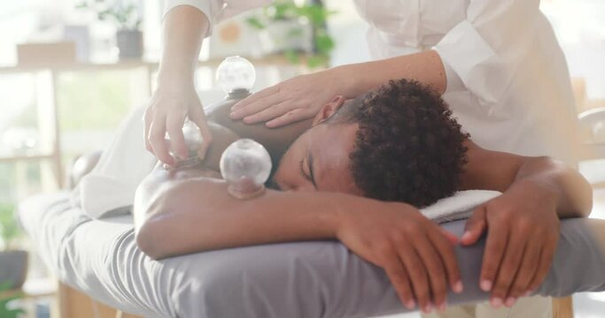 Young mixed race man enjoying relaxing and therapeutic back massage treatment with a vacuum cup in a spa. Beauty therapist treating body pain with suction cupping therapy to remove toxins