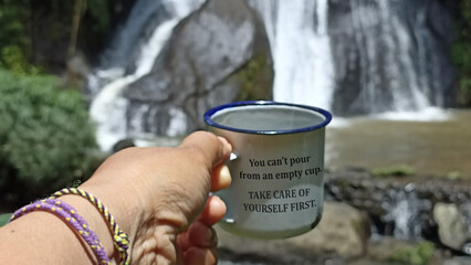 Inspirational quote - You can't pour from an empty cup. Take care of yourself first. With person holding traditional empty cup against the waterfall background. Self care and love concept. - obrazy, fototapety, plakaty