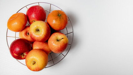 Ripe apples and tangerines in a metal basket on a white background