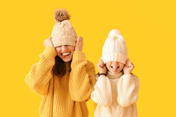 Funny little girl and her mother in warm hats and sweaters on yellow background