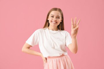 Young woman in t-shirt showing three fingers on pink background