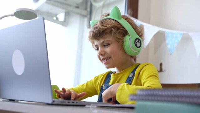 Cute smart caucasian primary School Child with headphones educate online laptop. Tutor teaching digital class, web lesson on computer at home. Virtual education course. Schoolboy girl studying doing